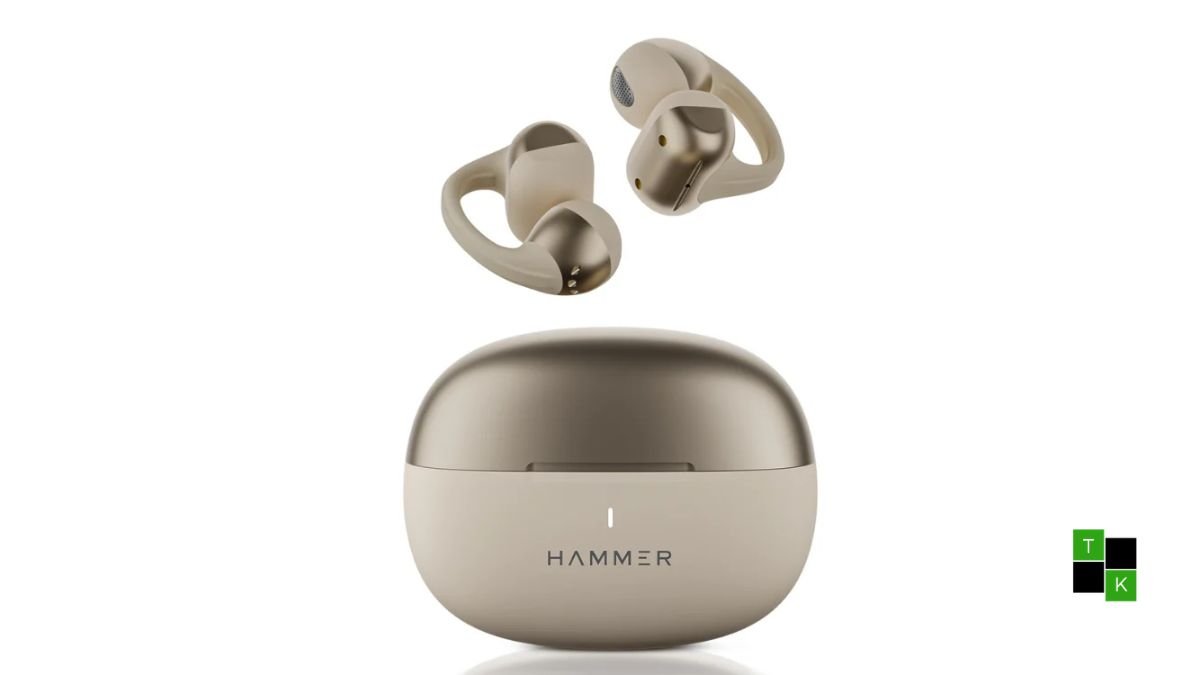 The Hammer Aura Air open-ear clip-on wireless earbuds in Champagne Gold resting beside their compact pebble charging case on a desk.