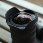 The compact Sony FE 8-14mm F3.5 G Fisheye zoom lens resting on a camera bag beside a Sony Alpha 7 mirrorless camera.