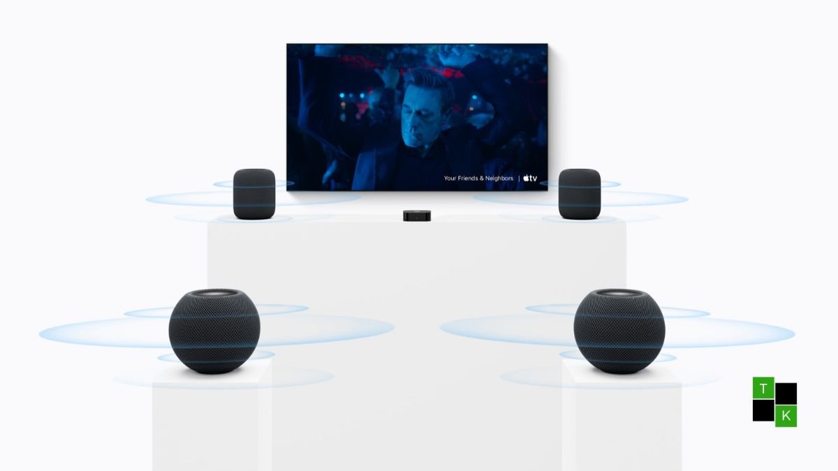 An original 2020 HomePod mini beside the new HomePod mini 2 displaying an illuminated Siri waveform on an architectural wooden console table.