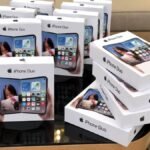 Apple iPhone Duo foldable smartphone in Star White resting opened on an architectural slate surface beside delivery delay metrics.